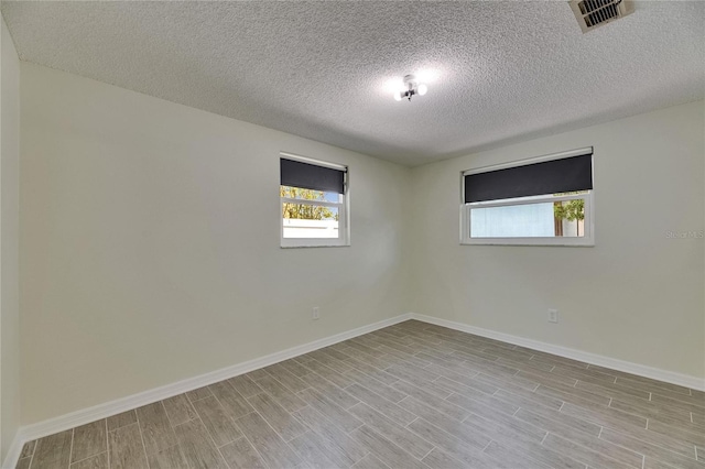 unfurnished room featuring visible vents, a textured ceiling, baseboards, and wood finished floors
