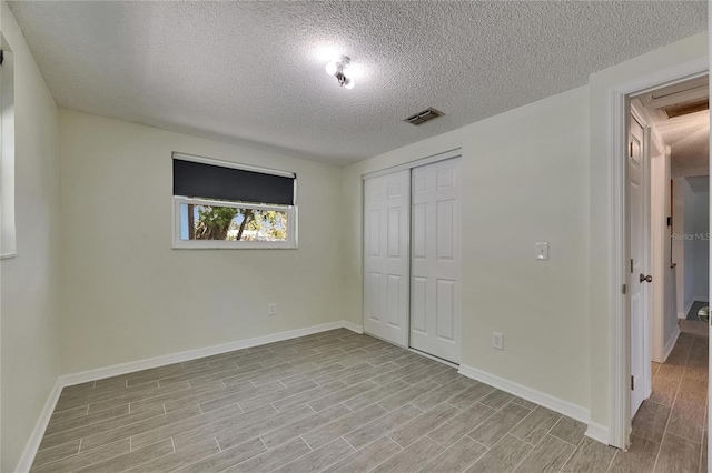 unfurnished bedroom with visible vents, a closet, baseboards, a textured ceiling, and light wood finished floors