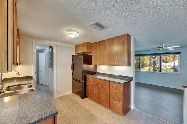 kitchen featuring freestanding refrigerator, a ceiling fan, dark countertops, baseboards, and a sink