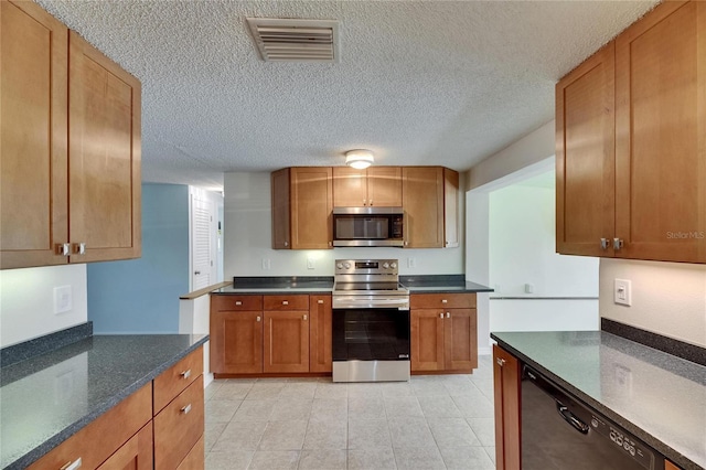 kitchen with visible vents, light tile patterned flooring, dark stone counters, a textured ceiling, and stainless steel appliances