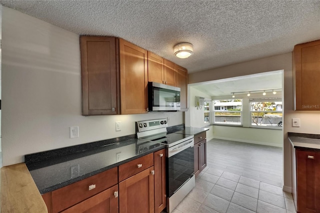 kitchen with a textured ceiling, rail lighting, appliances with stainless steel finishes, and light tile patterned floors