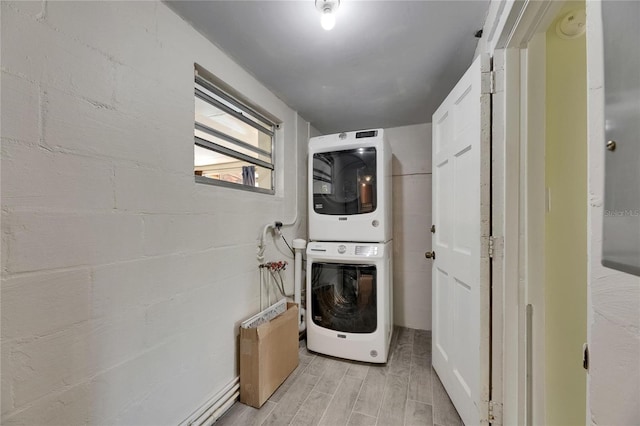 washroom with stacked washer / drying machine, light wood finished floors, and laundry area