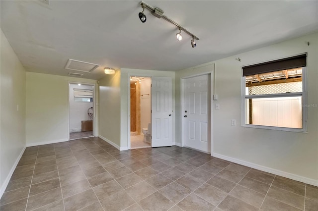 empty room featuring track lighting, baseboards, tile patterned flooring, and attic access