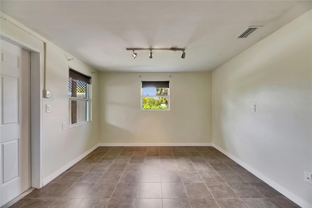 tiled empty room featuring rail lighting, visible vents, and baseboards