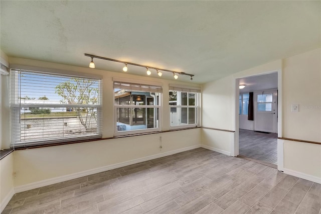 spare room featuring baseboards, rail lighting, and wood finished floors