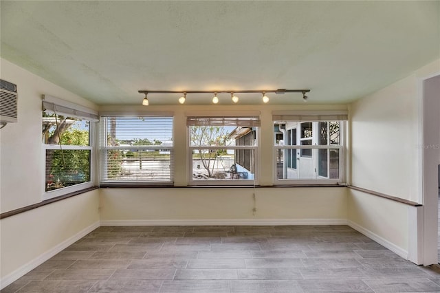 unfurnished sunroom featuring track lighting, baseboards, and an AC wall unit
