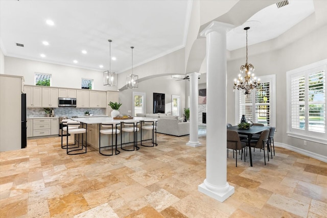 1600 Magnolia Rd, Belleair, FL 33756 - kitchen featuring appliances with stainless steel finishes, decorative columns, a towering ceiling, stone tile flooring, and a kitchen bar