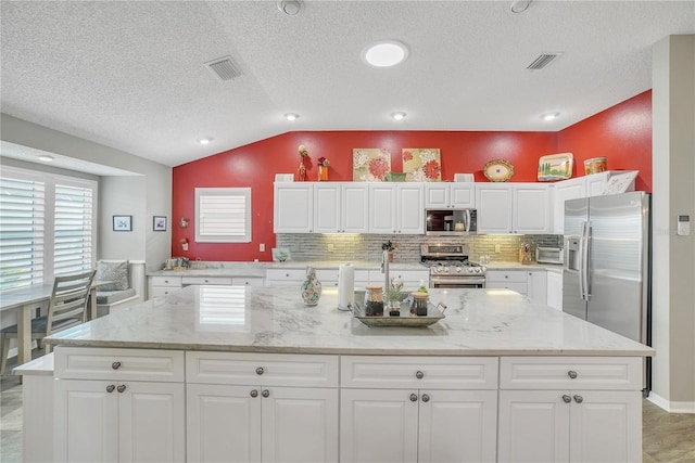 kitchen featuring decorative backsplash, appliances with stainless steel finishes, visible vents, a center island, and vaulted ceiling