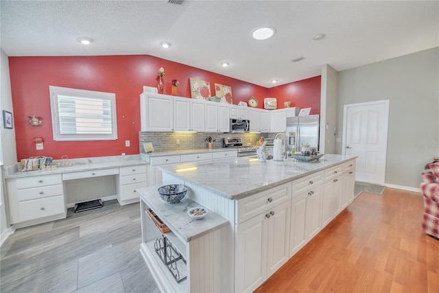 kitchen with tasteful backsplash, appliances with stainless steel finishes, white cabinetry, light wood-type flooring, and lofted ceiling