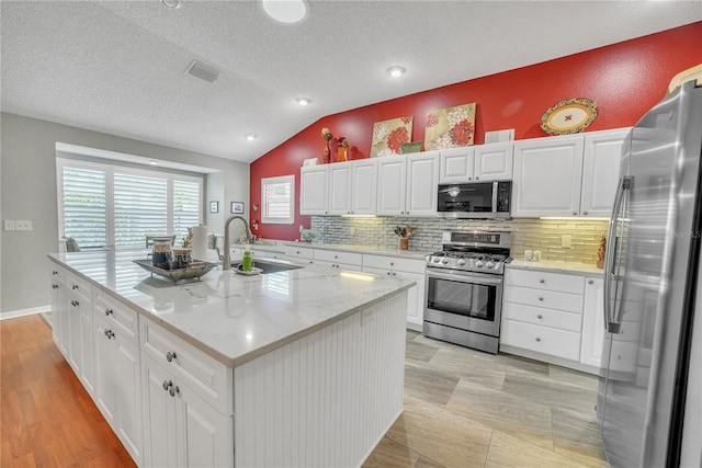 kitchen with decorative backsplash, vaulted ceiling, stainless steel appliances, and white cabinetry