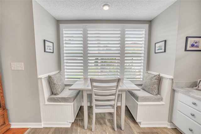 dining room featuring a textured ceiling, light wood-type flooring, and baseboards