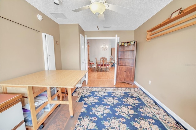 dining space with light wood finished floors, visible vents, baseboards, a textured ceiling, and ceiling fan with notable chandelier