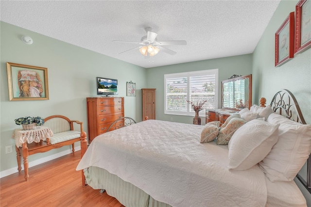 bedroom with a textured ceiling, ceiling fan, light wood-style flooring, and baseboards