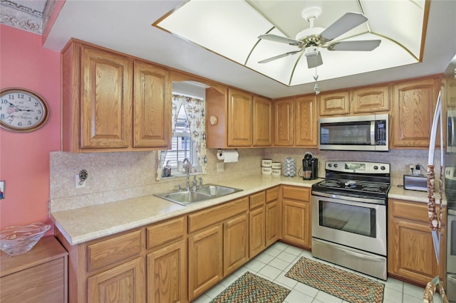 kitchen with a sink, stainless steel appliances, ceiling fan, backsplash, and light countertops