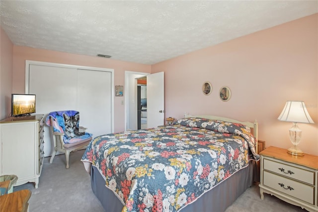 bedroom with light colored carpet, visible vents, a textured ceiling, and a closet