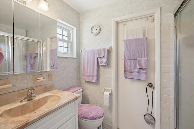 full bath with toilet, vanity, a shower stall, and wallpapered walls