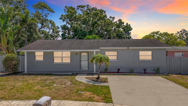 ranch-style home with fence, roof with shingles, and a lawn