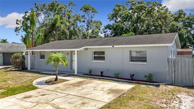 ranch-style house with stucco siding, roof with shingles, a front yard, fence, and brick siding