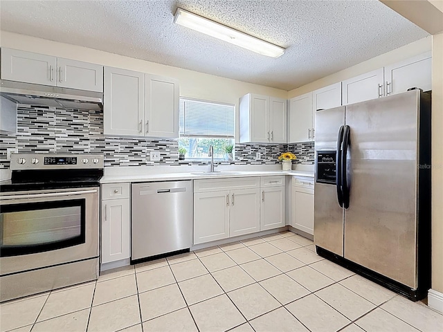 kitchen with a sink, under cabinet range hood, light countertops, a textured ceiling, and appliances with stainless steel finishes