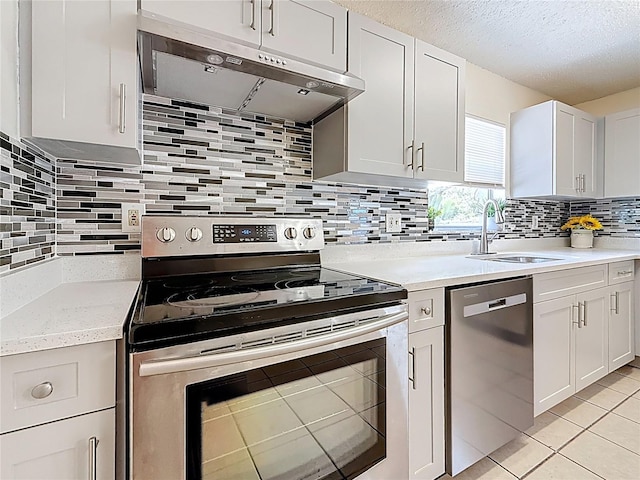 kitchen featuring a sink, under cabinet range hood, light tile patterned flooring, tasteful backsplash, and appliances with stainless steel finishes