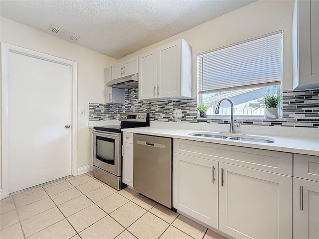 kitchen featuring stainless steel appliances, under cabinet range hood, light countertops, a sink, and visible vents