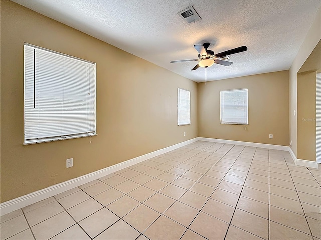 unfurnished room with a textured ceiling, light tile patterned floors, visible vents, baseboards, and a ceiling fan
