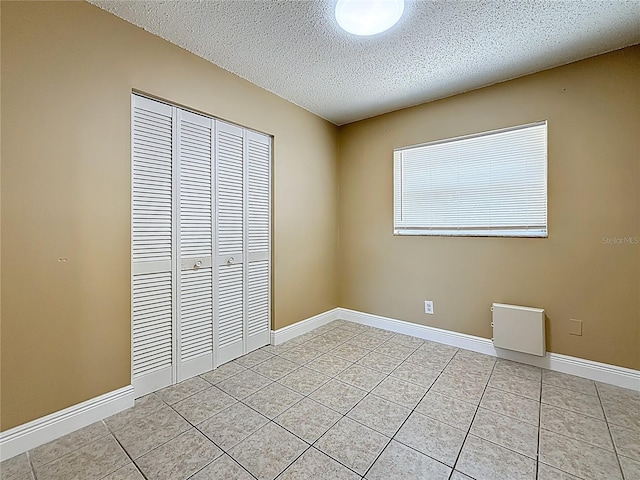 unfurnished bedroom featuring baseboards, light tile patterned floors, a textured ceiling, and a closet