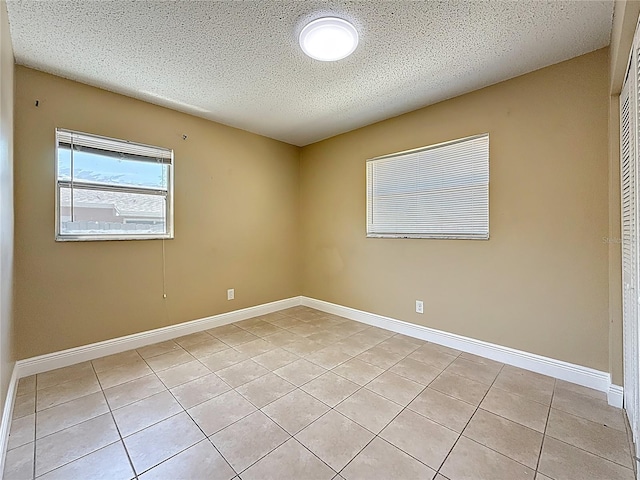 empty room featuring baseboards, light tile patterned floors, and a textured ceiling