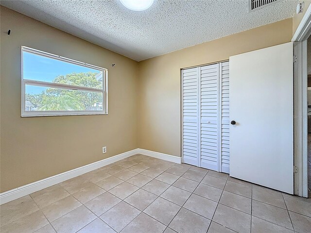 unfurnished bedroom featuring a textured ceiling, visible vents, a closet, baseboards, and light tile patterned flooring
