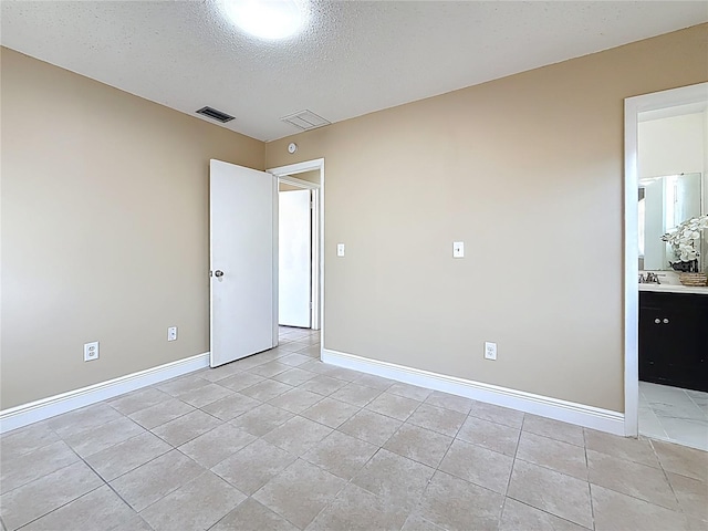 spare room with baseboards, visible vents, light tile patterned floors, and a textured ceiling