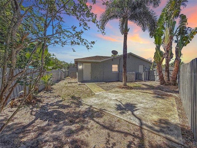 back of house at dusk featuring stucco siding, a gate, a patio, and a fenced backyard
