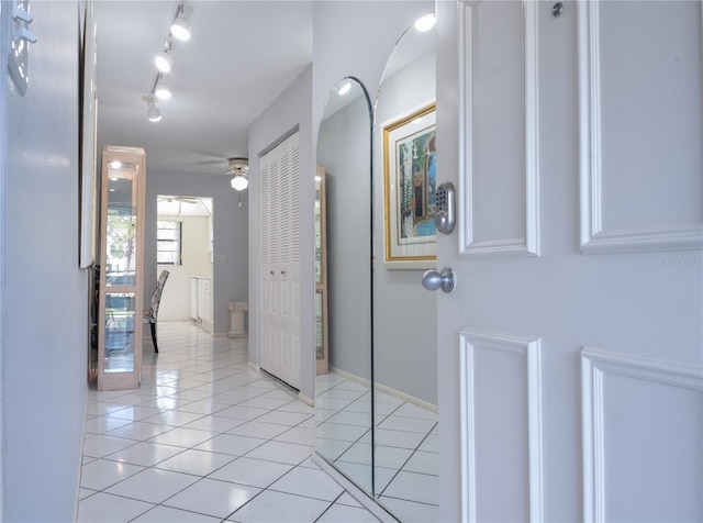 corridor with rail lighting, light tile patterned flooring, and baseboards