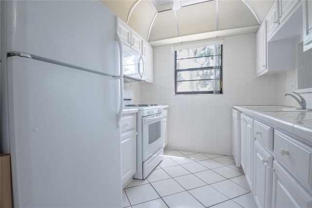 kitchen with tile walls, a sink, tile countertops, white appliances, and white cabinets