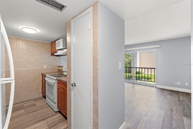 kitchen featuring visible vents, light wood finished floors, under cabinet range hood, and white appliances