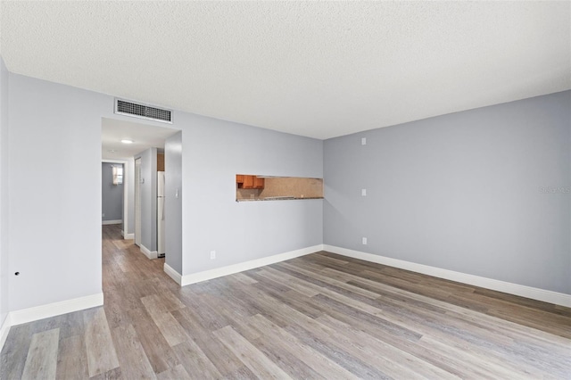 empty room with a textured ceiling, baseboards, wood finished floors, and visible vents
