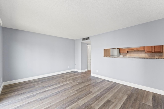 unfurnished living room featuring visible vents, a textured ceiling, baseboards, and wood finished floors