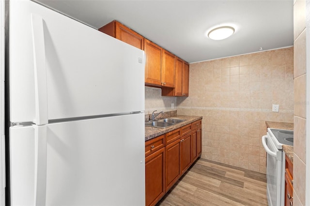 kitchen with brown cabinetry, tile walls, a sink, light wood-style floors, and white appliances