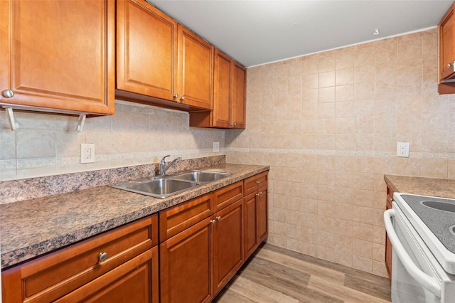 kitchen featuring a sink, light wood finished floors, brown cabinetry, tile walls, and white electric stove