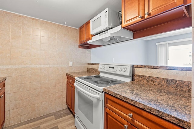 kitchen featuring brown cabinetry, white appliances, tile walls, light wood-type flooring, and under cabinet range hood