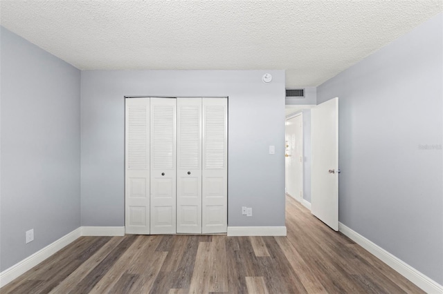 unfurnished bedroom with baseboards, visible vents, wood finished floors, and a closet