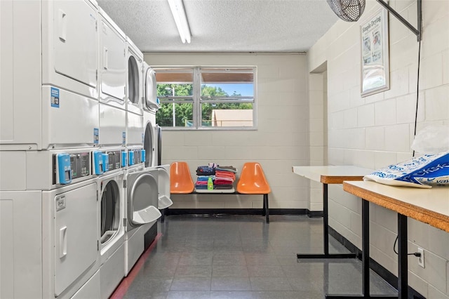 common laundry area featuring washing machine and clothes dryer, concrete block wall, a textured ceiling, and stacked washer and clothes dryer