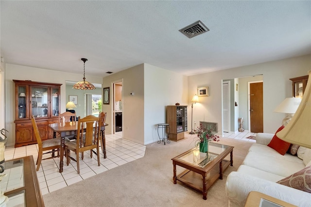 living room featuring visible vents, a textured ceiling, light tile patterned flooring, and light colored carpet