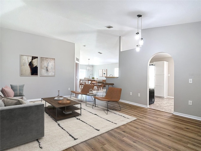living area with wood finished floors, baseboards, visible vents, and arched walkways