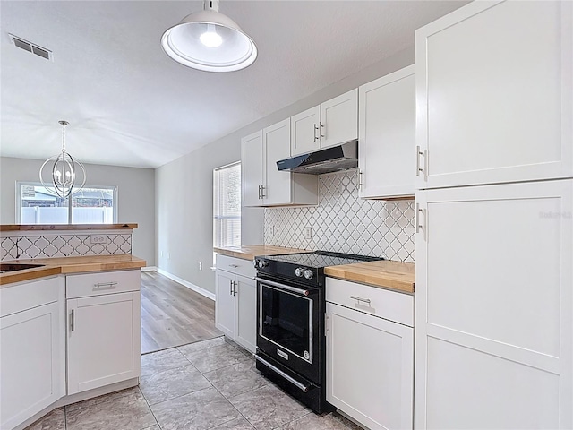 kitchen with wood counters, under cabinet range hood, decorative backsplash, black / electric stove, and white cabinetry