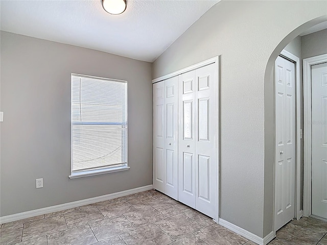 unfurnished bedroom featuring lofted ceiling, two closets, baseboards, and arched walkways