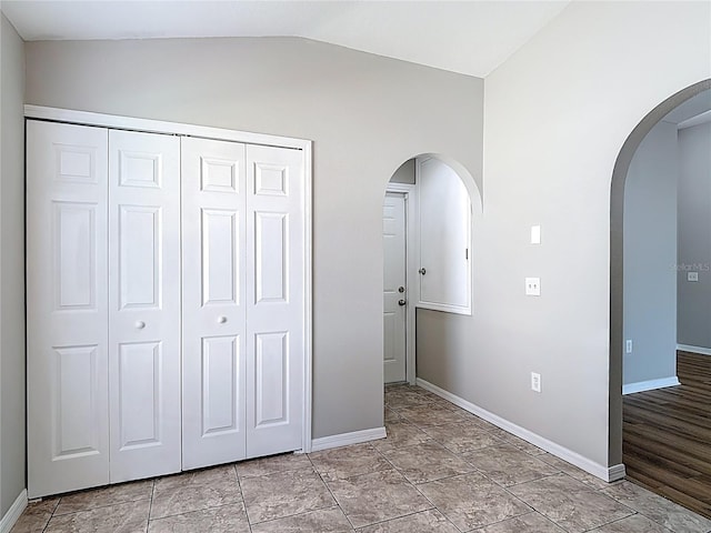 unfurnished bedroom with baseboards, arched walkways, a closet, and lofted ceiling