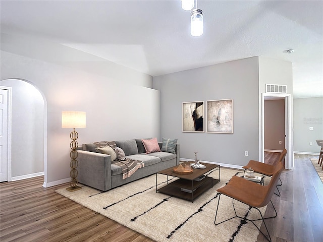 living room featuring wood finished floors, visible vents, baseboards, and arched walkways