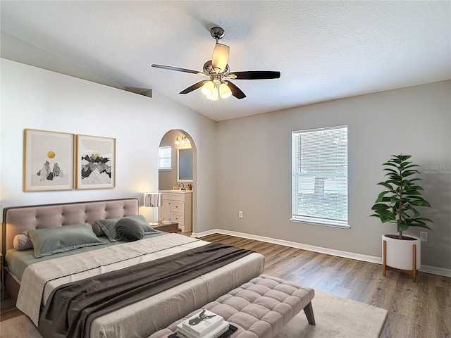 bedroom with light wood-type flooring, arched walkways, multiple windows, and vaulted ceiling
