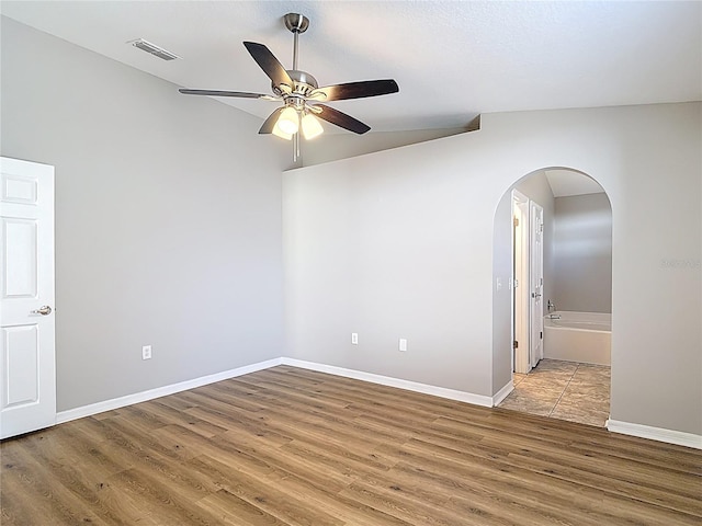 spare room featuring visible vents, ceiling fan, baseboards, arched walkways, and wood finished floors