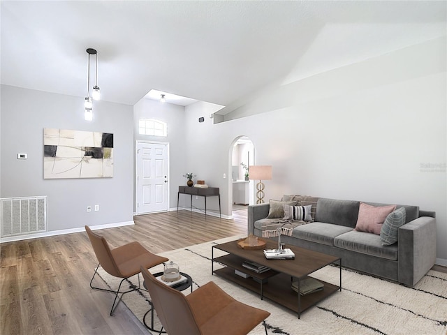 living area featuring visible vents, baseboards, arched walkways, wood finished floors, and high vaulted ceiling